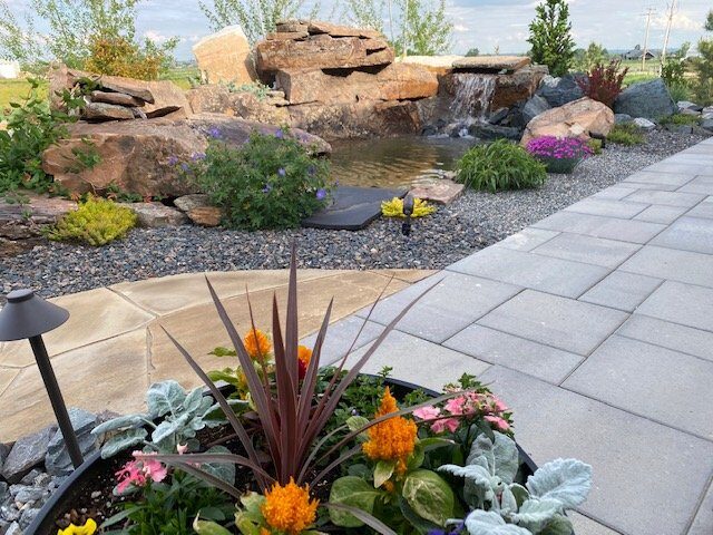 Boulder waterfall and pondless water feature next to a paver patio by Brooks Landscape