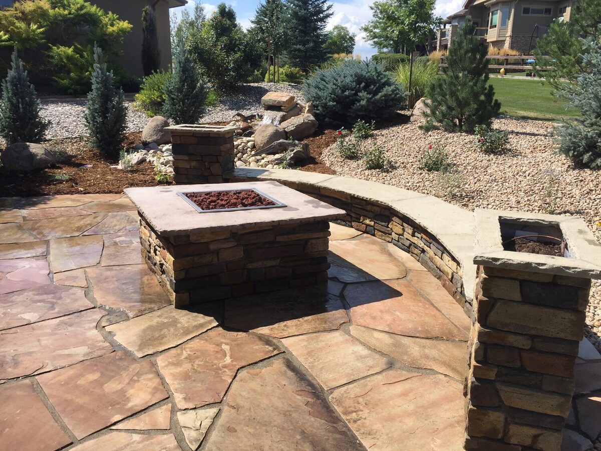Flagstone patio with a square stone fire pit and curved seat wall by Brooks Landscape